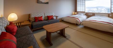 A hotel room with a sofa, two beds, tatami flooring, a wooden table, and a city view through large windows.