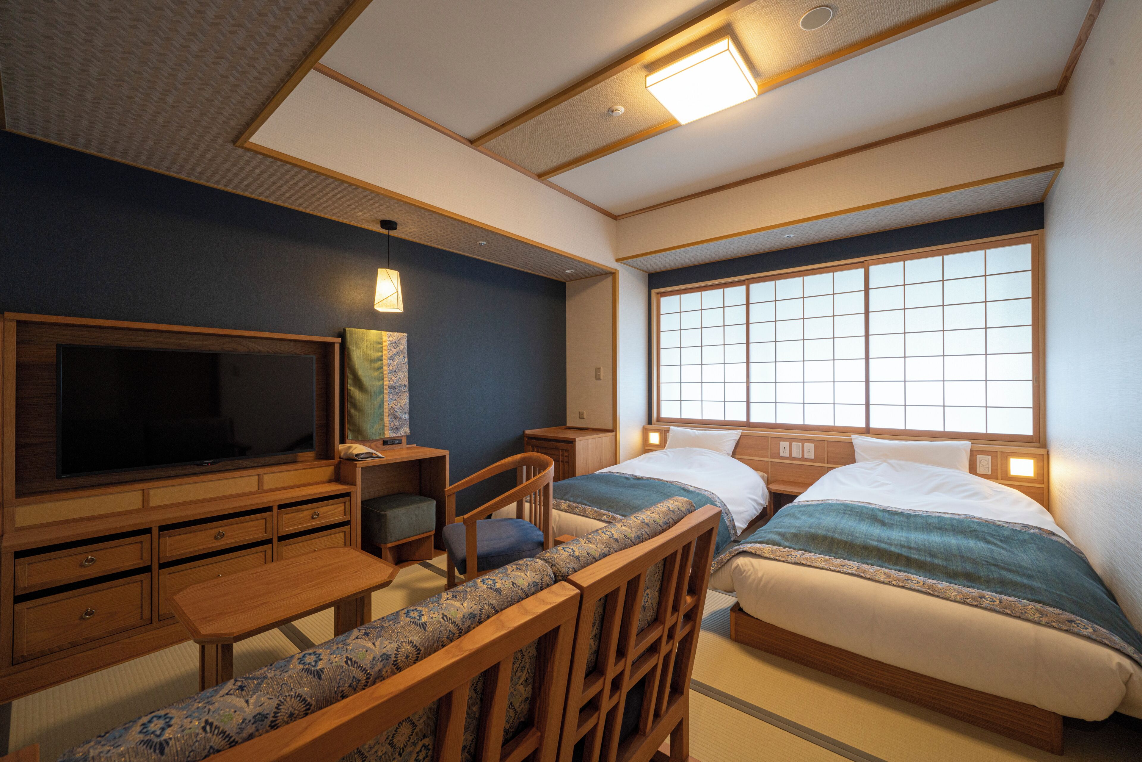 A traditional Japanese-style room with tatami flooring, a television, a desk, and two beds with shoji screens.