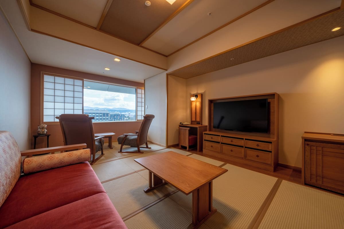A living room with tatami flooring, a sofa, a TV, and a view of the city.