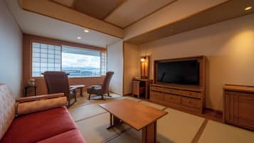 A living room with tatami flooring, a sofa, a TV, and a view of the city.