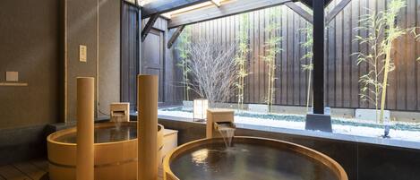A traditional Japanese onsen with wooden tubs and a bamboo tree in the background.