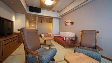 A traditional Japanese-style room with tatami flooring, a television, a sofa, two chairs, and a small table.