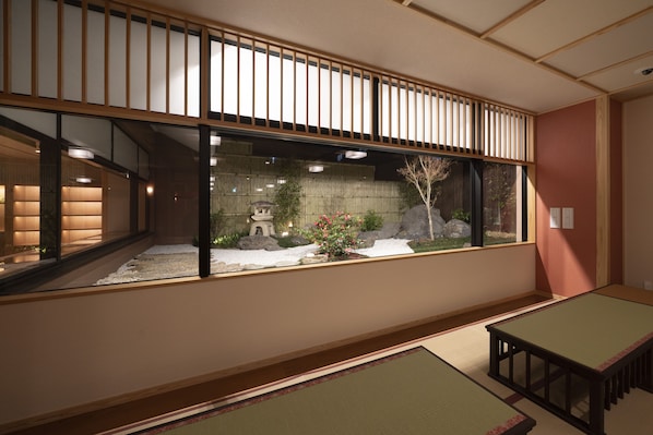 Una habitación japonesa tradicional con suelo de tatami, una mesa baja y vistas a un jardín con un farol de piedra y cerezos en flor.