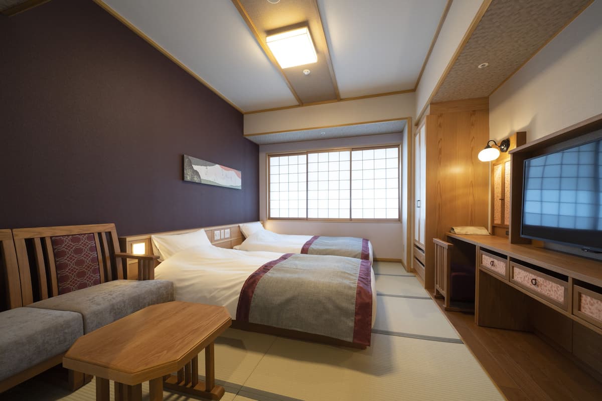 A hotel room with two beds, a sofa, a TV, and a small table.