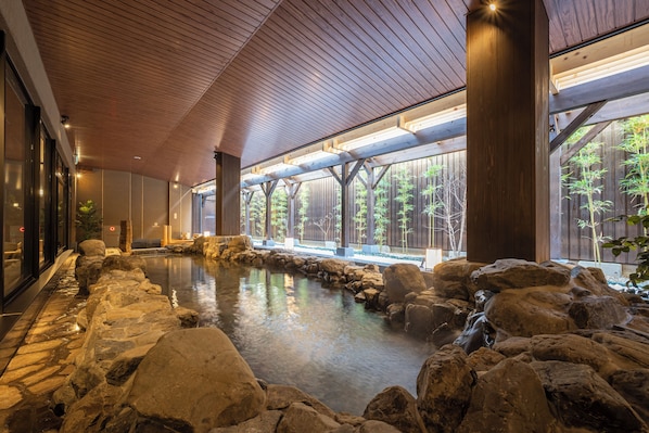 Un área de spa con piscina bordeada de rocas, vigas de madera y ventanas amplias.
