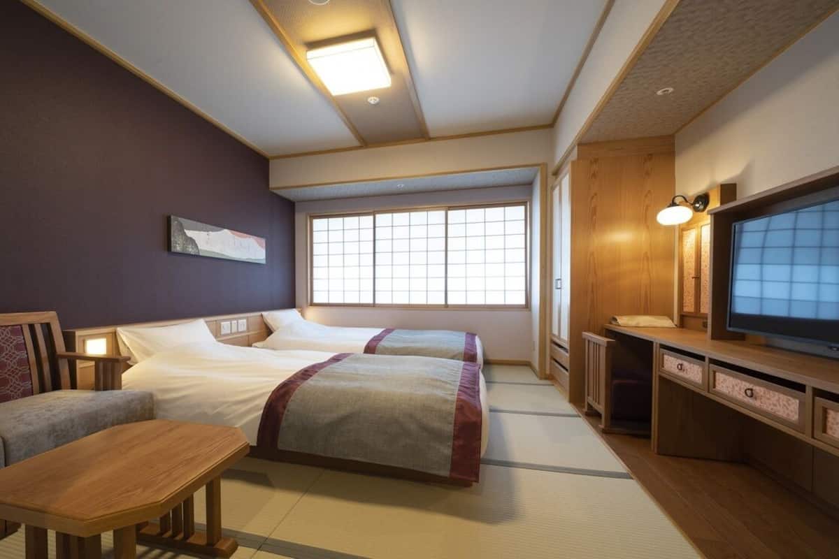 A hotel room with two beds, a sofa, a TV, and a desk.