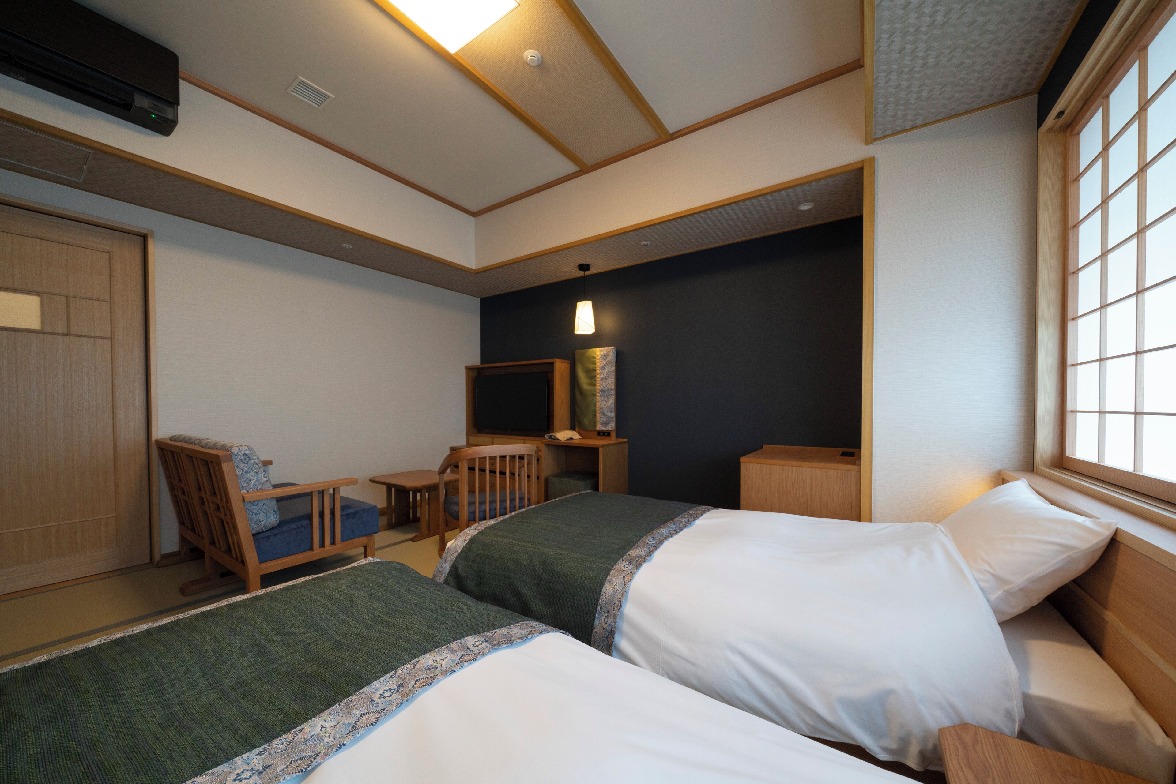 A hotel room with two beds, a desk, a chair, a wardrobe, and a window.