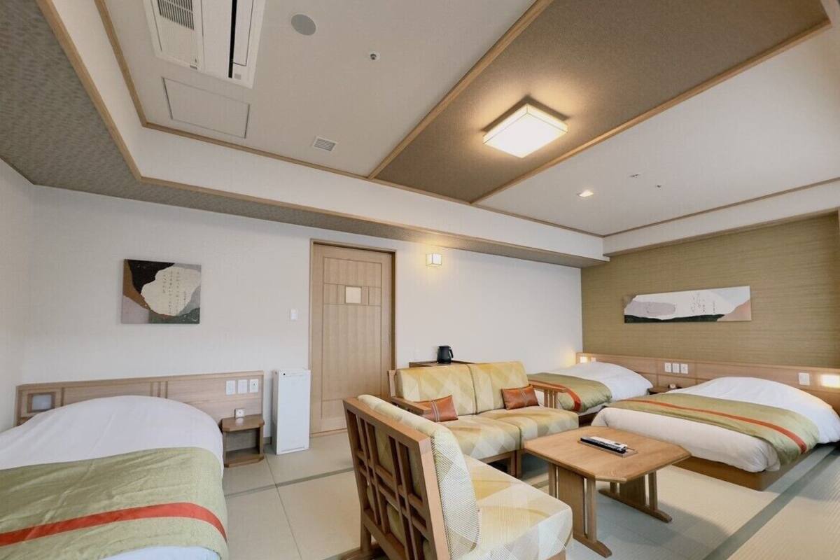 A hotel room with a bed, a sofa, a chair, a small table, and a nightstand.