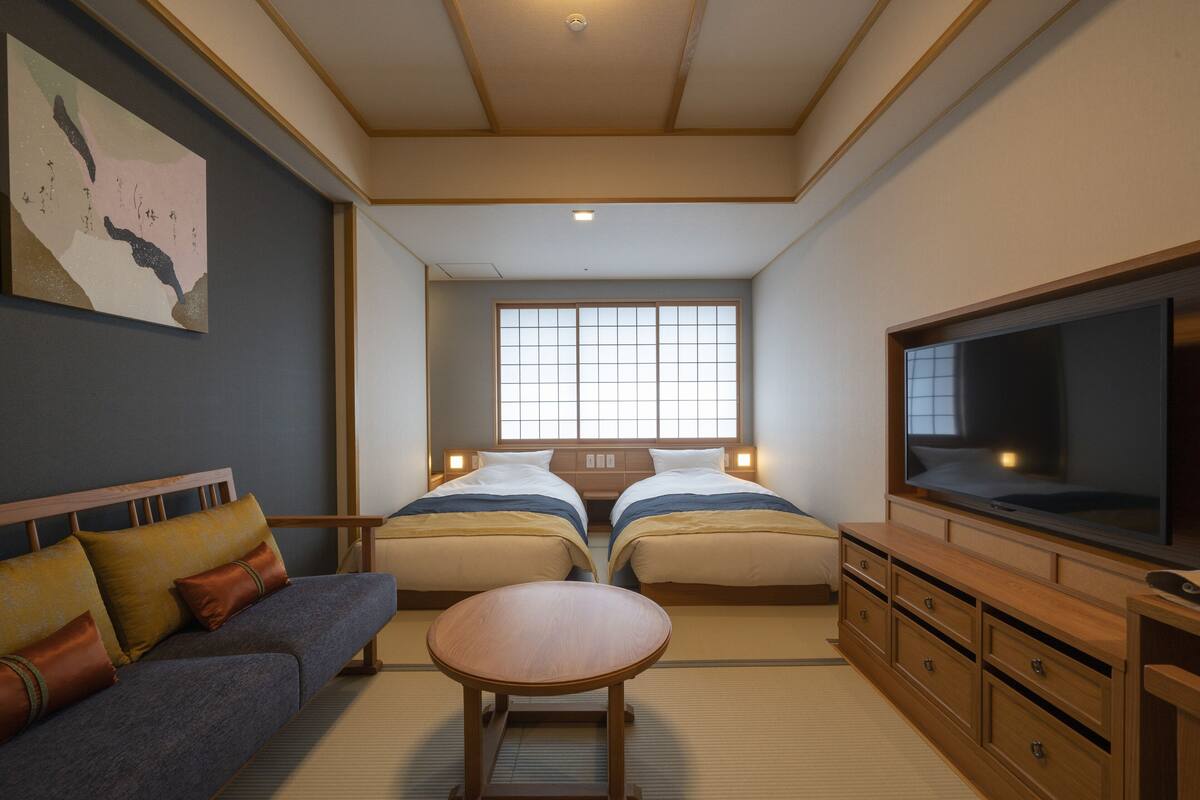 A hotel room with two beds, a sofa, a TV, and a tatami mat floor.