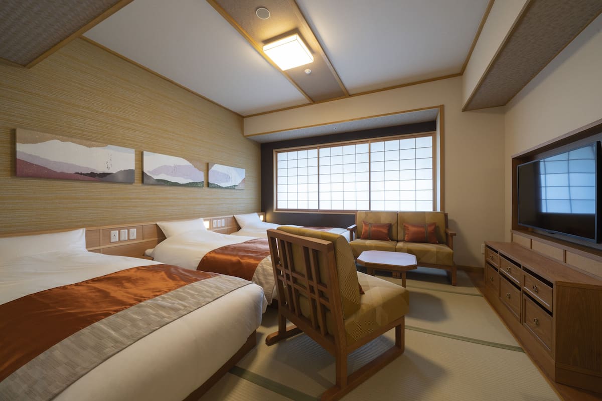 A hotel room with two beds, a sofa, a TV, and artwork on the wall.