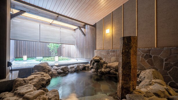 A hot spring area with a stone wall, wooden ceiling, and a view of a garden outside. - Kyoto Umekoji Kadensho (Kyoto)