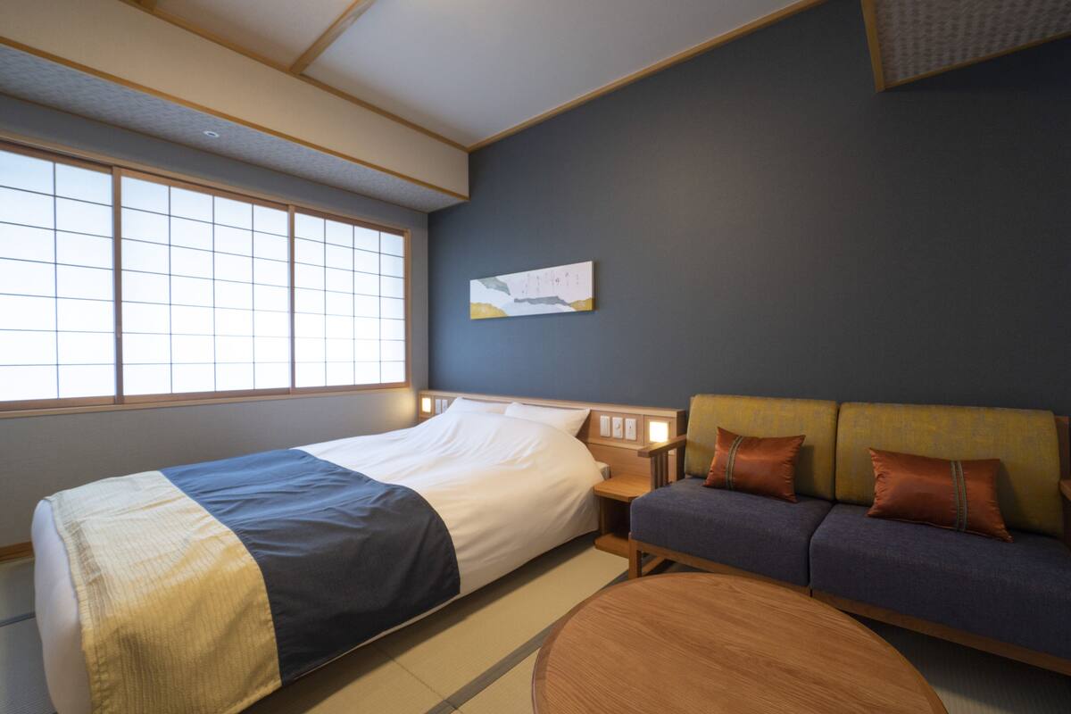 A hotel room with a large bed, a sofa, a round coffee table, and a window with a view.