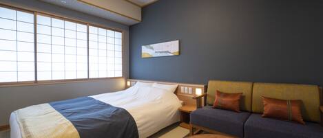 A hotel room with a large bed, a sofa, a round coffee table, and a window with a view.