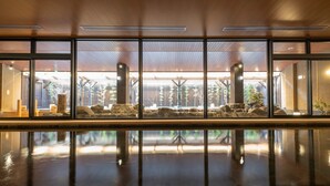 A spacious indoor area with large windows, a stone water feature, and wooden ceiling beams.