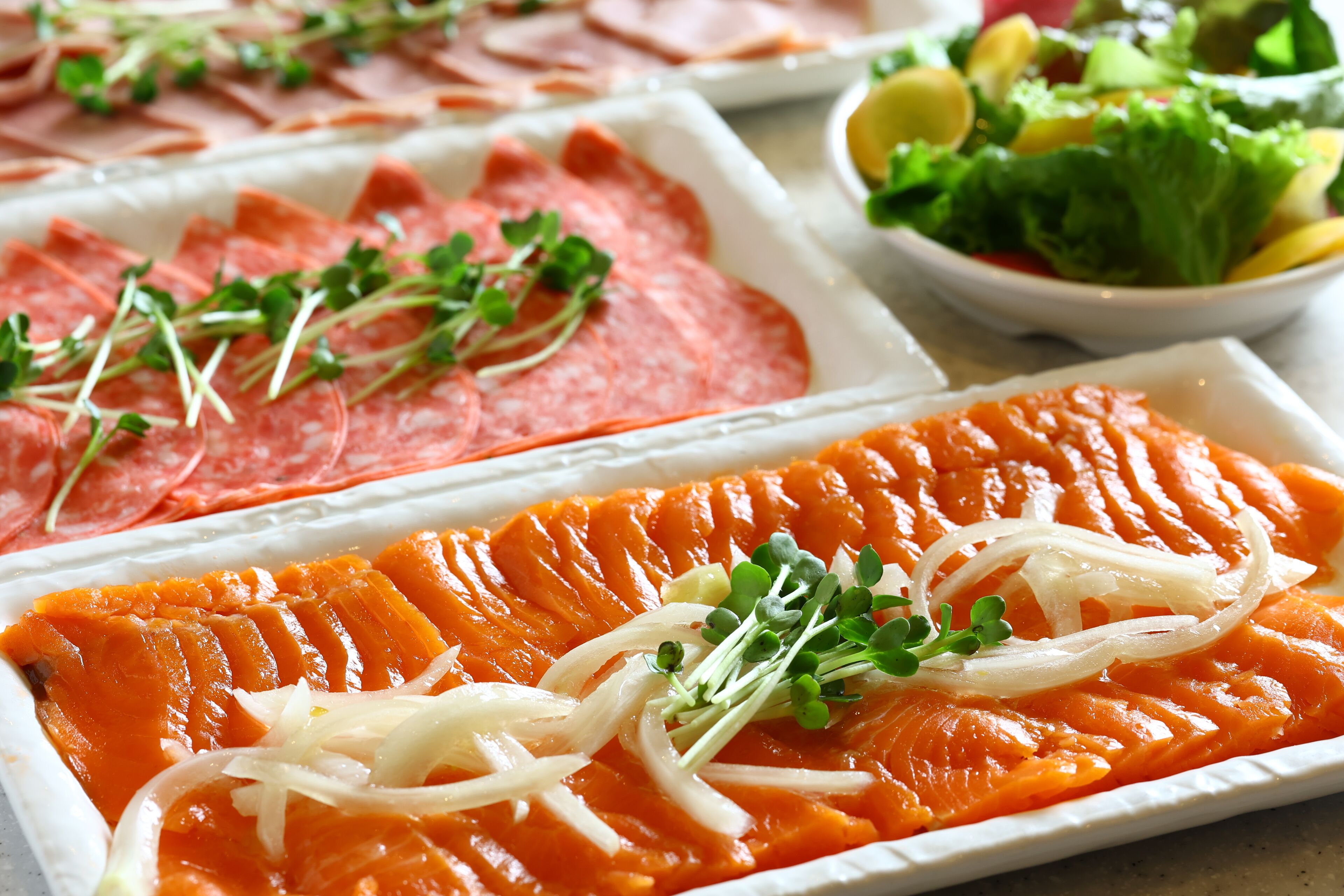 A variety of food items including sliced salmon, ham, and a salad.