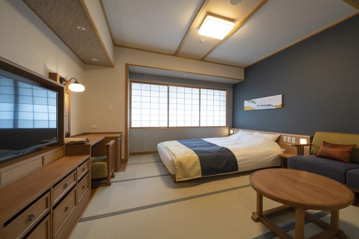 A hotel room with a bed, a sofa, a TV, a desk, and a window.
