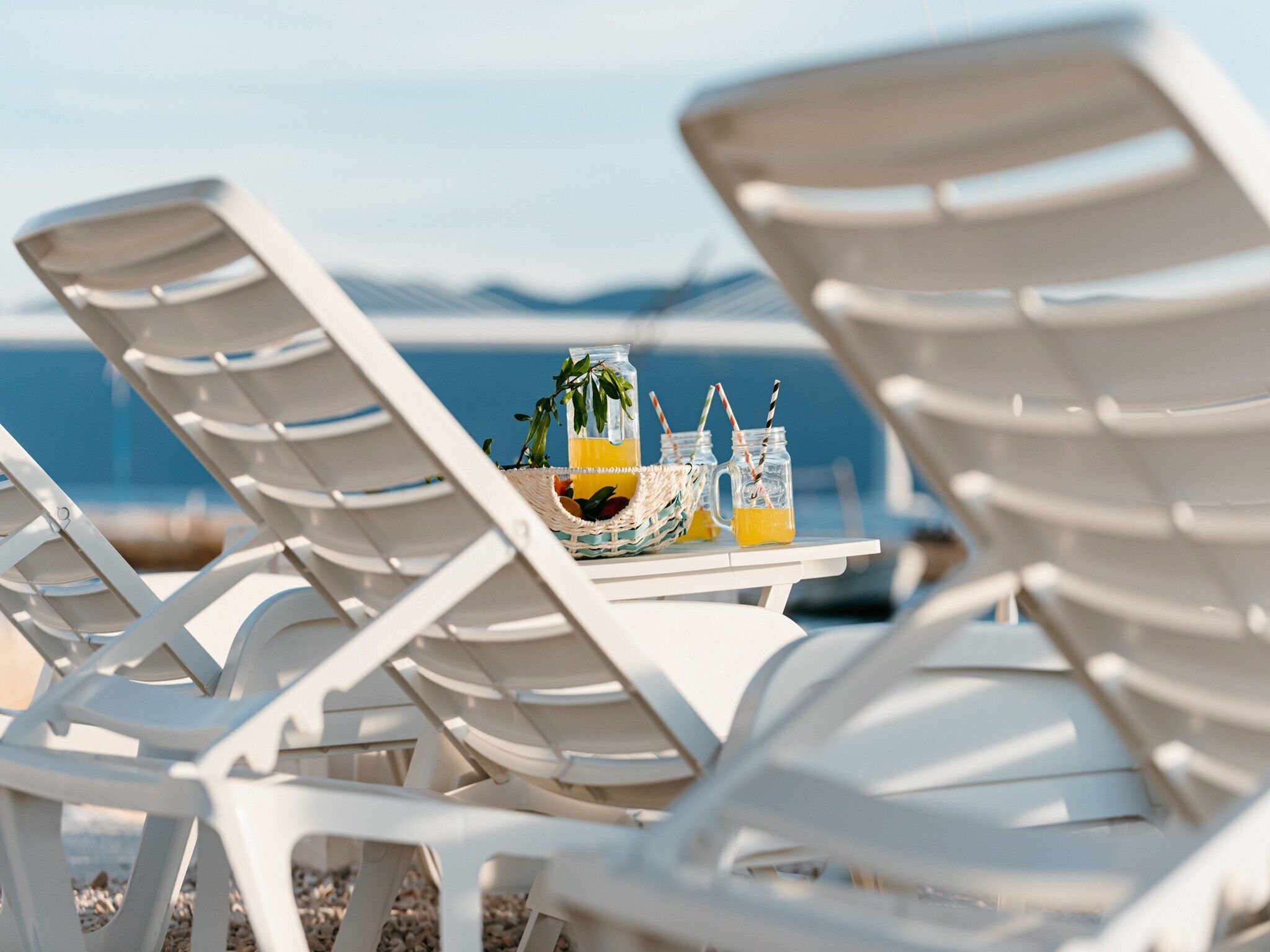 White lounge chairs, a table with drinks, and a view of the sea.