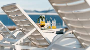 White lounge chairs, a table with drinks, and a view of the sea.