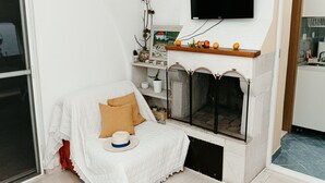 A cozy living room with a fireplace, a television mounted above it, and a comfortable seating area with a sofa and cushions. - Apartments Dragobratović (Slivno)