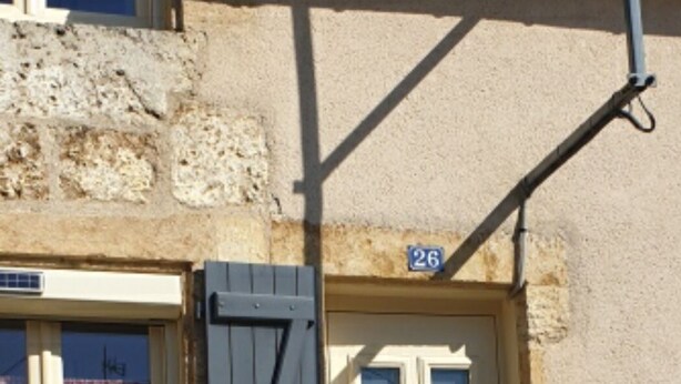 A stone building with a white door, a blue shutter, and a number '26' sign.