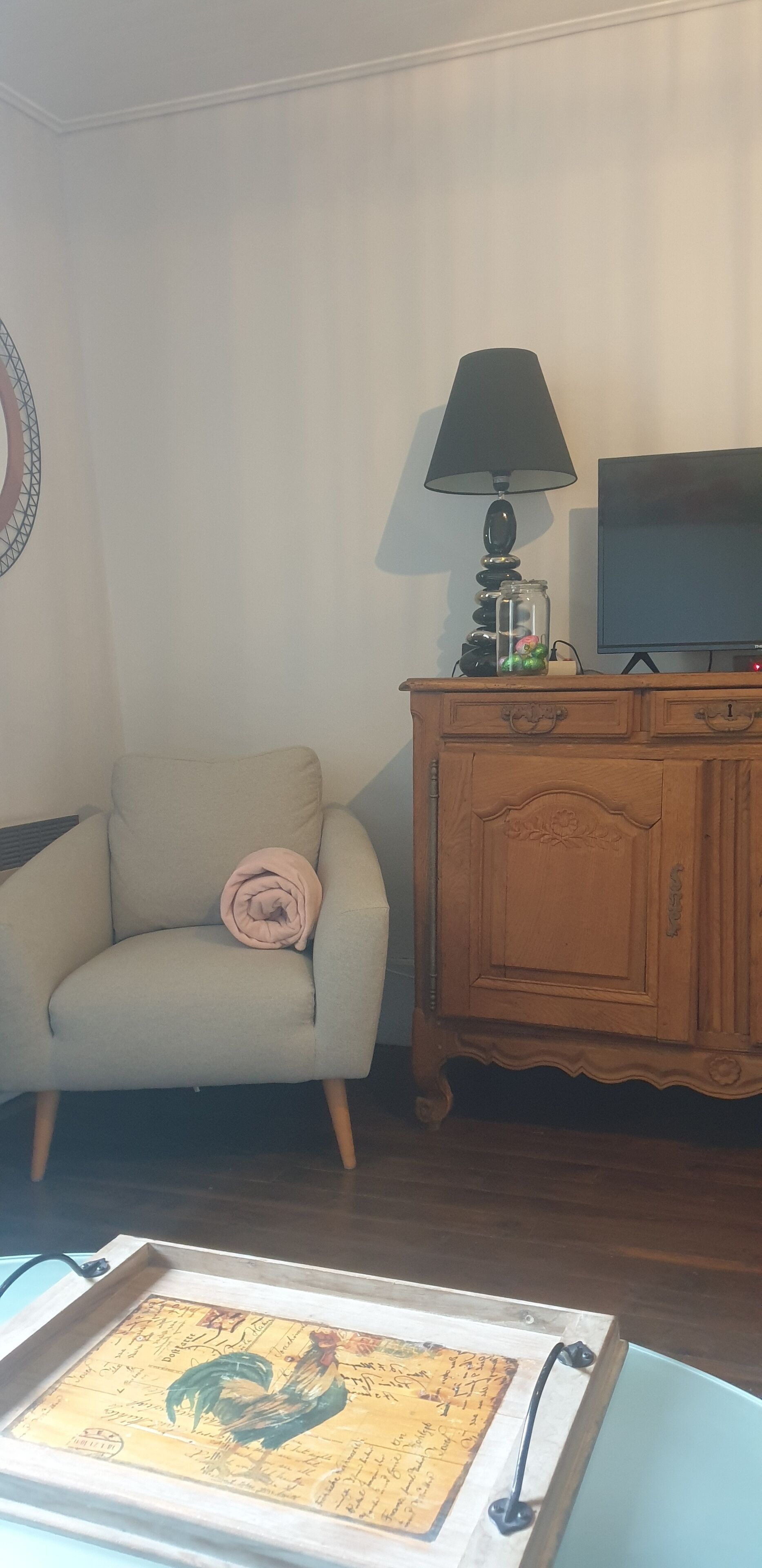 A living room with a beige armchair, a wooden cabinet, a television, and a lamp.