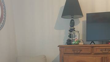 A living room with a beige armchair, a wooden cabinet, a television, and a lamp.