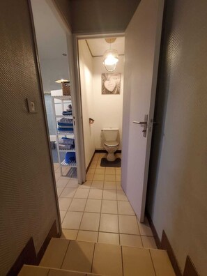 A narrow hallway leading to a bathroom with a toilet and a wall-mounted light fixture. - Chez Émile Logement Entier, 2 Chambres, Jardin Privé (Hûmes)