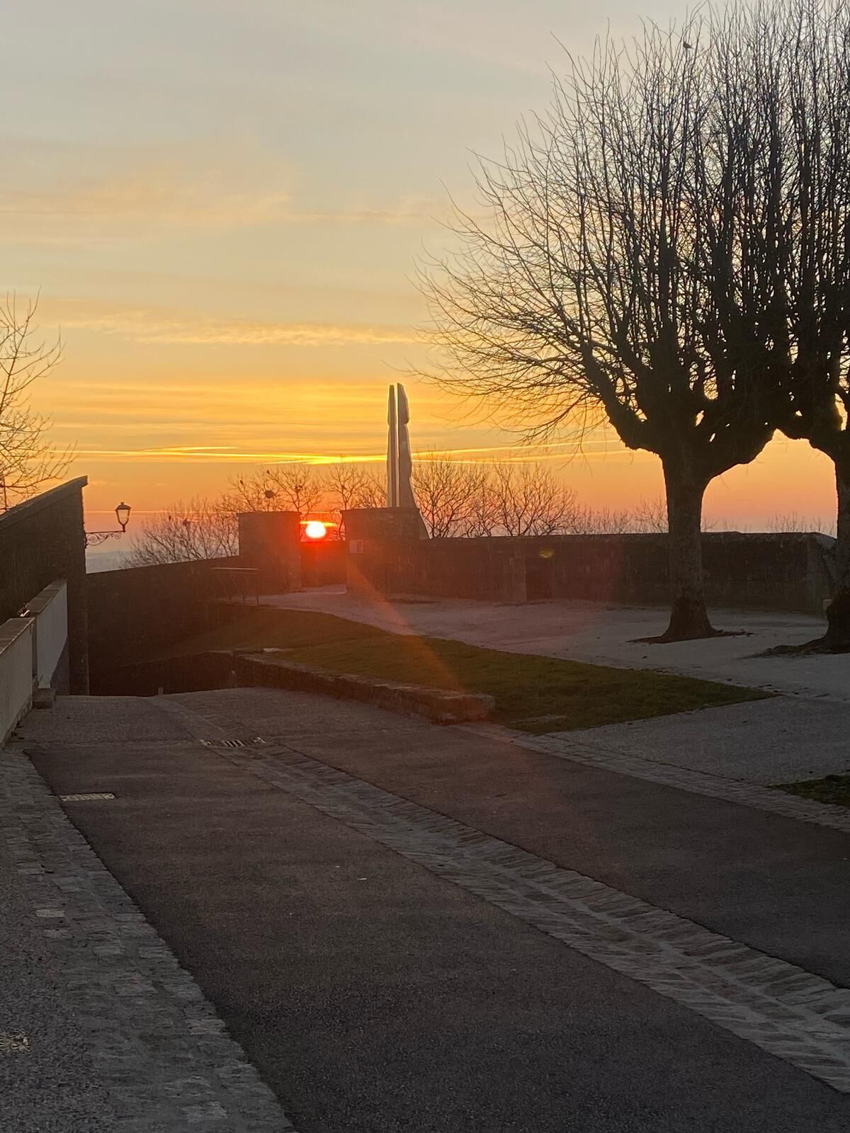 Vista do pôr do sol com uma estátua e uma árvore em primeiro plano.
