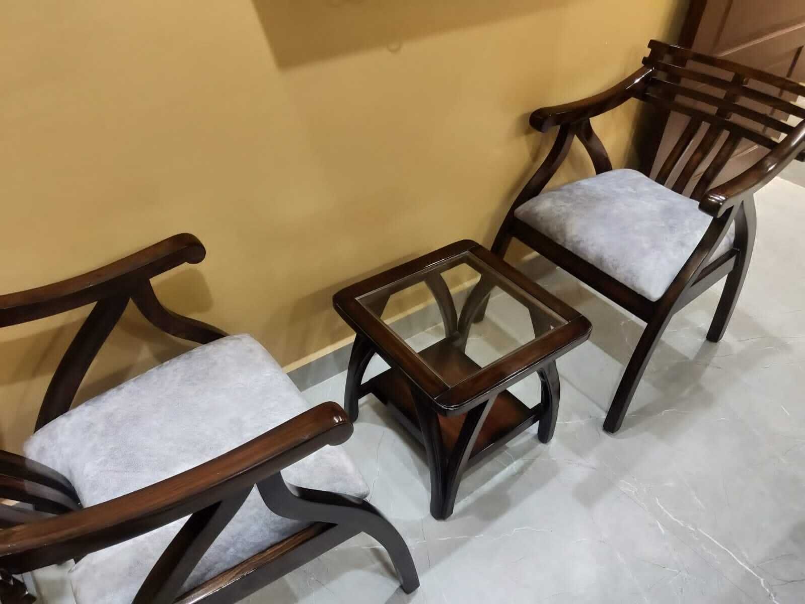 Un ensemble de chaises en bois avec des assises rembourrées et une petite table en verre placée entre elles.