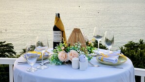 Tavolo imbandito per due, con bottiglia di vino, bicchieri e un centrotavola decorativo, vista mare.