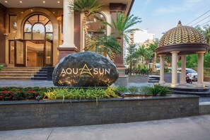 A hotel entrance with a large rock sign, palm trees, and a gazebo.