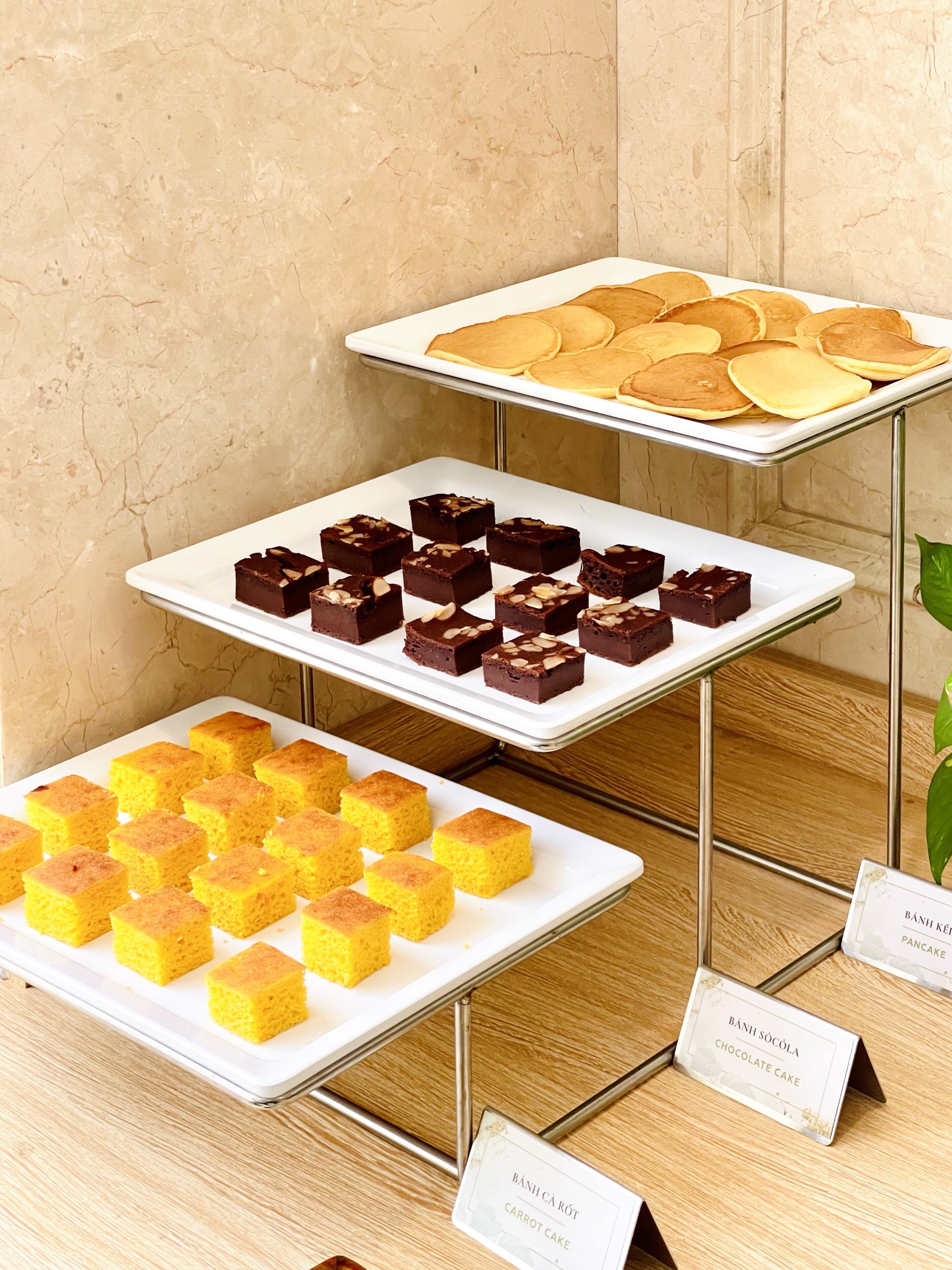 A dessert display with trays of pancakes, brownies, and a yellow cake, each labeled with their names.
