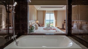 Un bagno moderno con una vasca da bagno ampia, una doccia e vista su una camera da letto con un letto e tende.