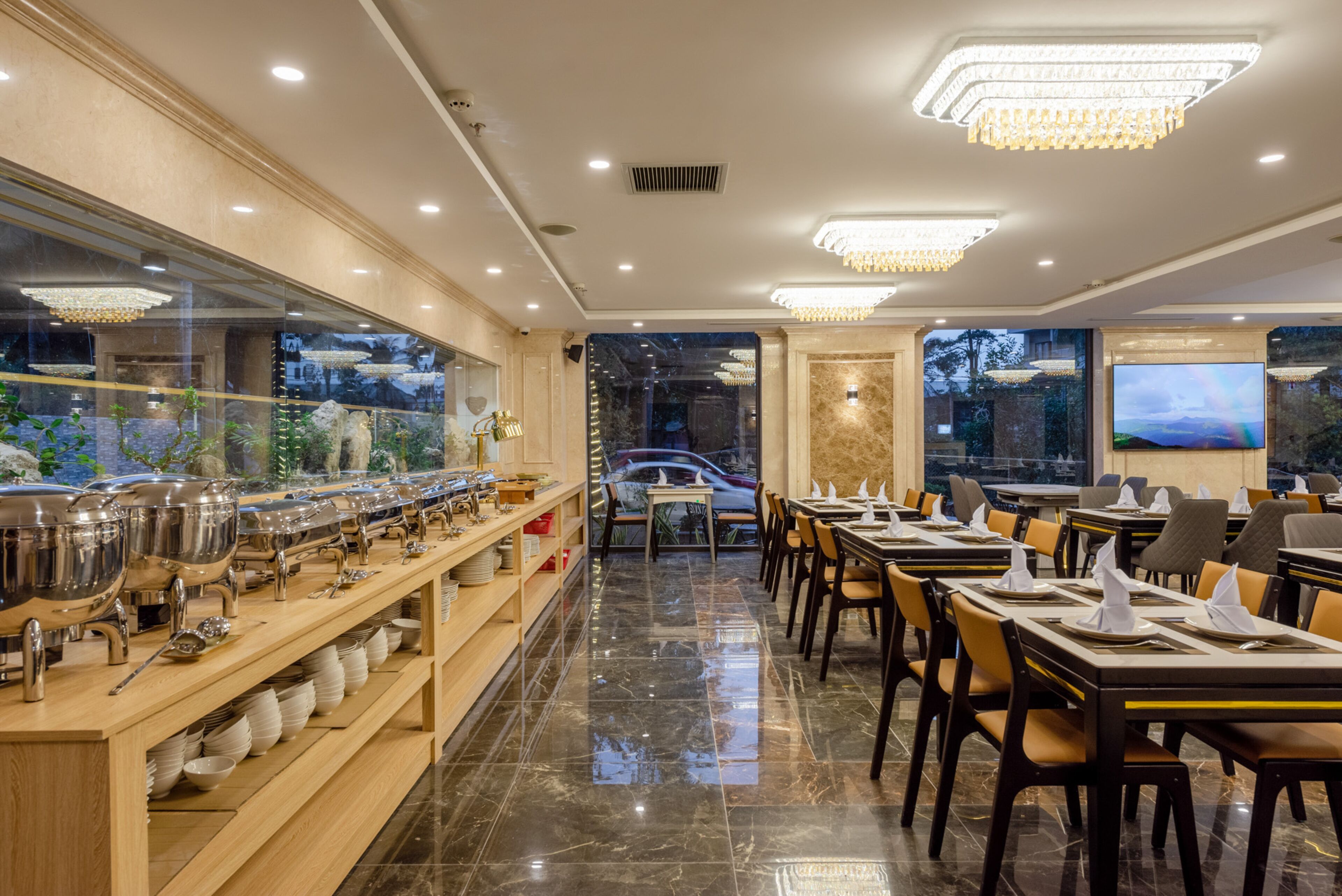 A restaurant with a long buffet line, neatly arranged tables, and a chandelier.