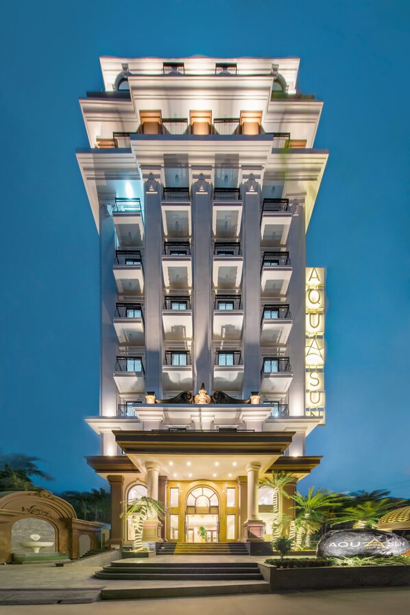 Un hotel de varios pisos con un llamativo letrero 'AQUA', con balcones, una entrada imponente y una fachada bien iluminada.
