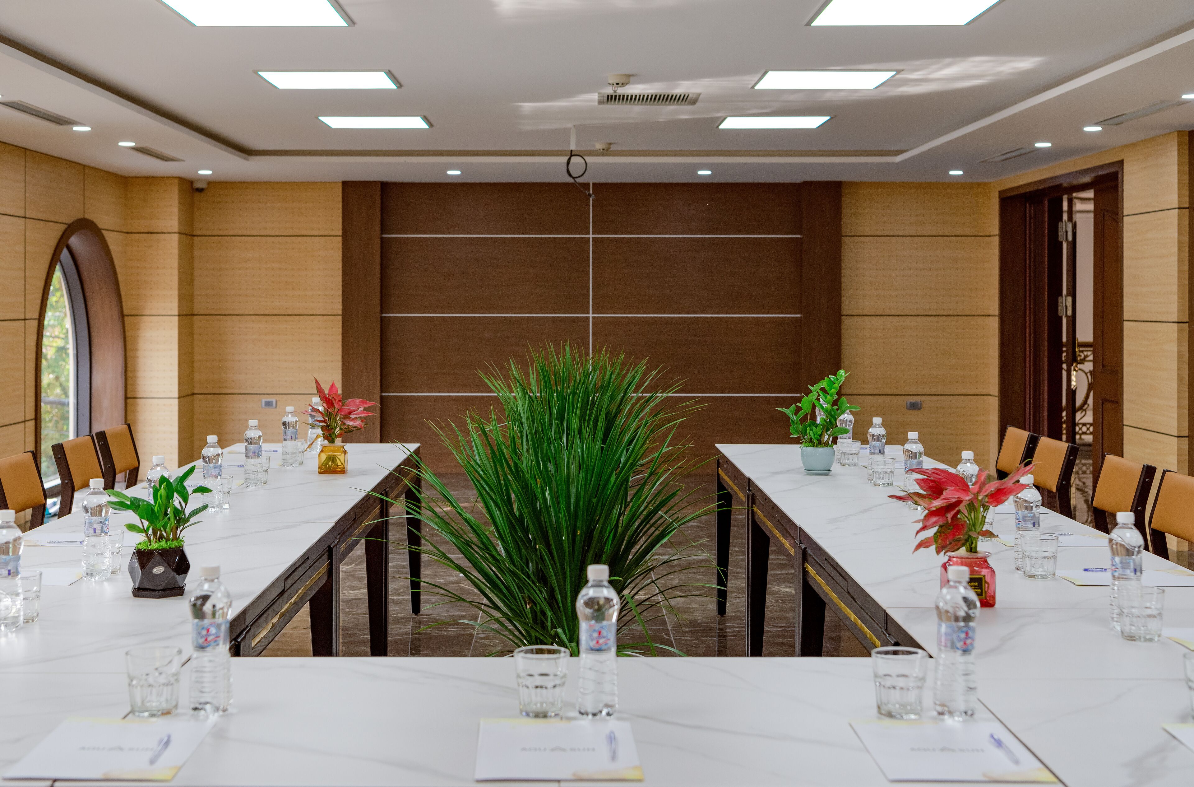 A conference room with a long table, chairs, water bottles, and potted plants.
