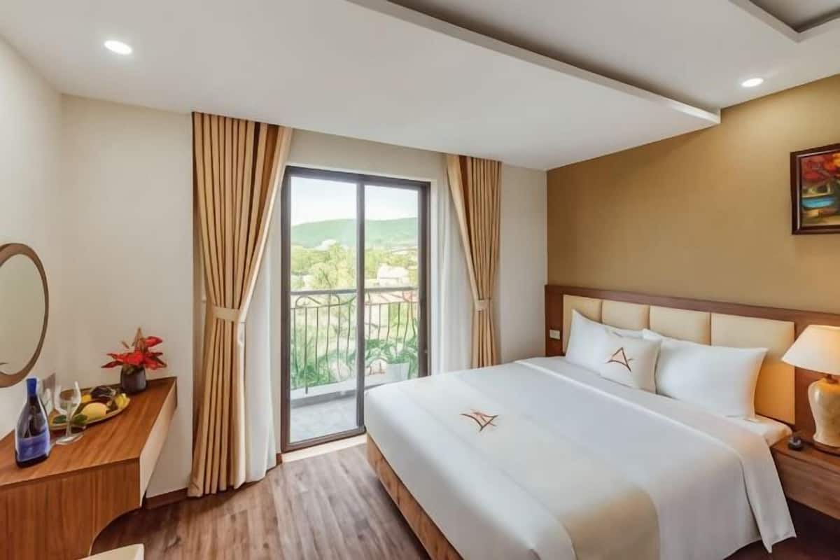 Hotelkamer met een bed, een bureau met spiegel, een nachtkastje en uitzicht door een glazen deur.