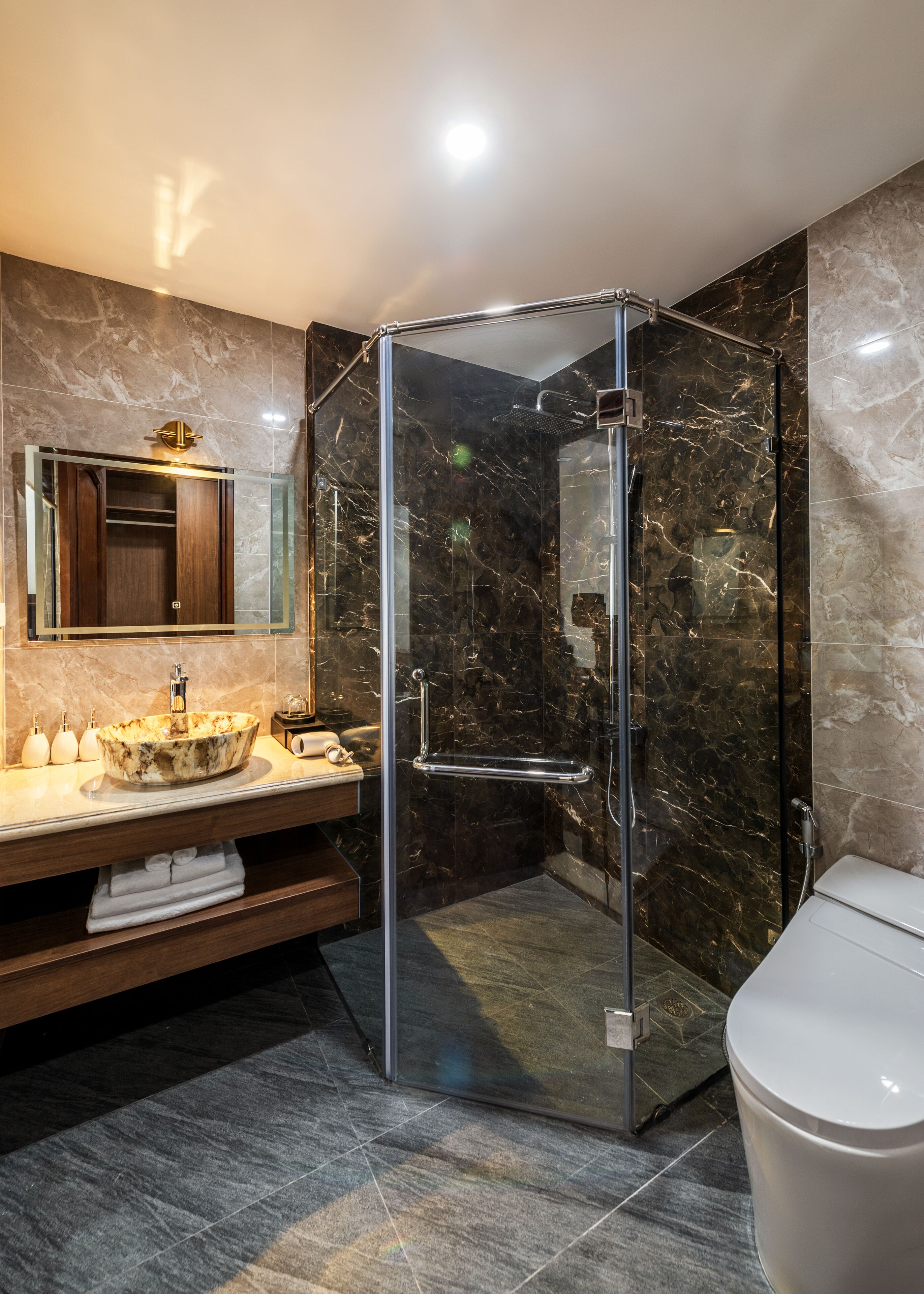 A modern bathroom with a glass-enclosed shower, a marble vanity, and a toilet.