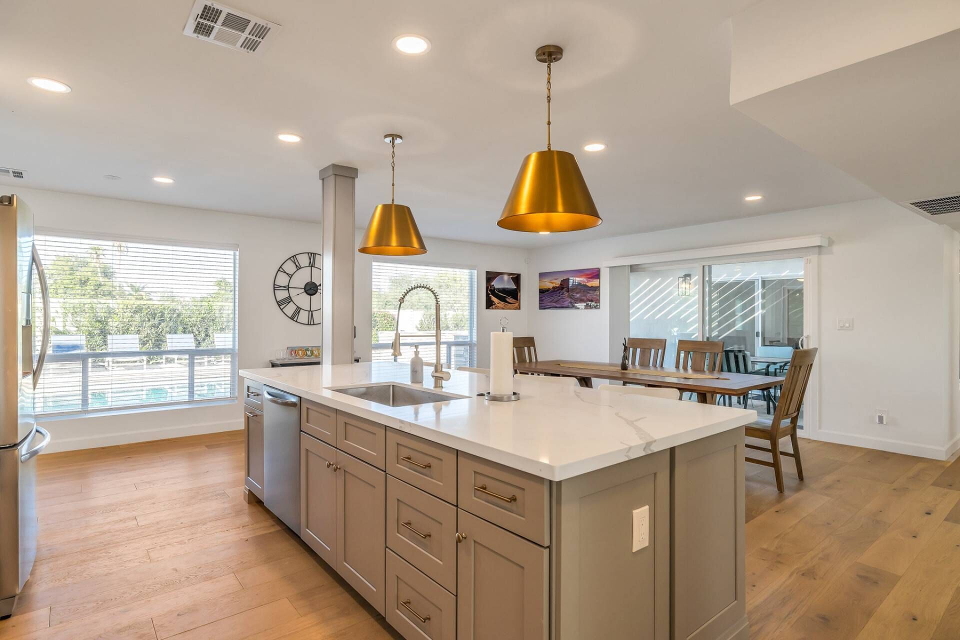 A modern kitchen with a central island, pendant lighting, and a dining area with wooden chairs.