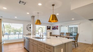 Una cocina moderna con una isla central, iluminación colgante y una zona de comedor con sillas de madera.
