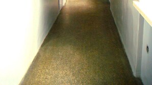 A narrow, carpeted hallway with white walls and a wooden door at the end. - HOSTEL OMEGA (Rzeszów)