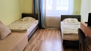 A small, clean room with two single beds, a wooden floor, a desk with a chair, and a window with curtains. - HOSTEL OMEGA (Rzeszów)