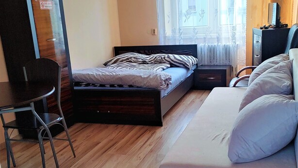 A bedroom with a bed, a sofa, a desk, a wardrobe, and a window with curtains. - HOSTEL OMEGA (Rzeszów)