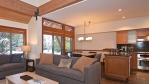 A modern living room with a grey sofa, a coffee table with a book, and a dining area with a wooden table and chairs.