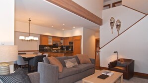 A modern living room with a grey sofa, a coffee table, and a staircase with decorative wall art.