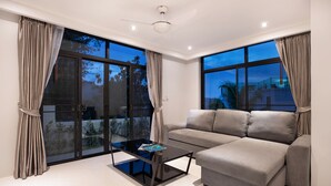 A modern living room with a sectional sofa, a glass coffee table, and large windows offering a view of the outdoors. - King Size Sea View Villa + Pool + Rooftop Skydeck  (Kathu)