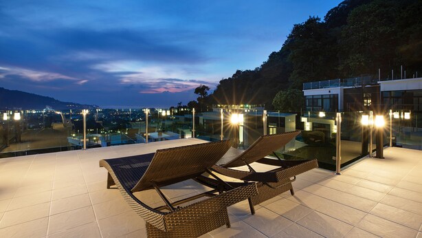 A rooftop terrace with lounge chairs and a glass balustrade overlooking a cityscape at dusk. - King Size Sea View Villa + Pool + Rooftop Skydeck  (Kathu)