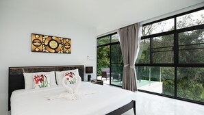 A modern bedroom with a large bed, a decorative wall piece, and a view of a lush garden through large windows. - King Size Sea View Villa + Pool + Rooftop Skydeck  (Kathu)