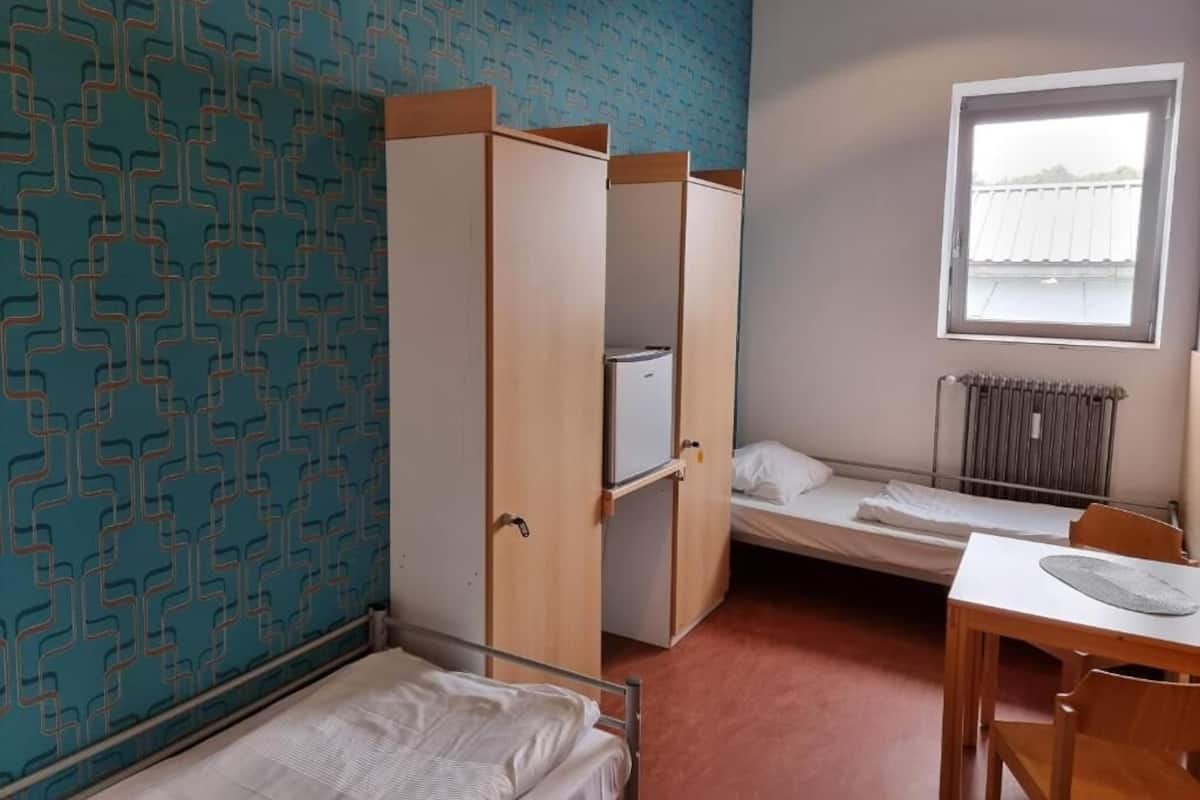 A small, single-room accommodation with a bunk bed, a desk, and a window.
