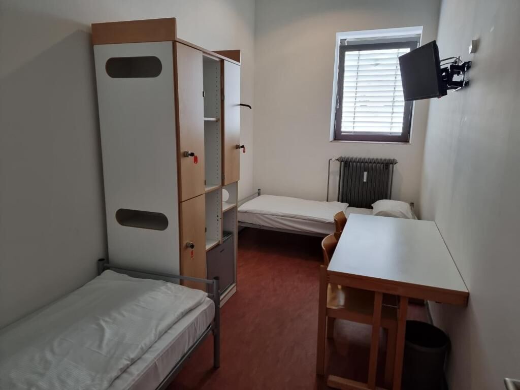 A compact room with a bunk bed, a desk, a chair, a radiator, and a window.